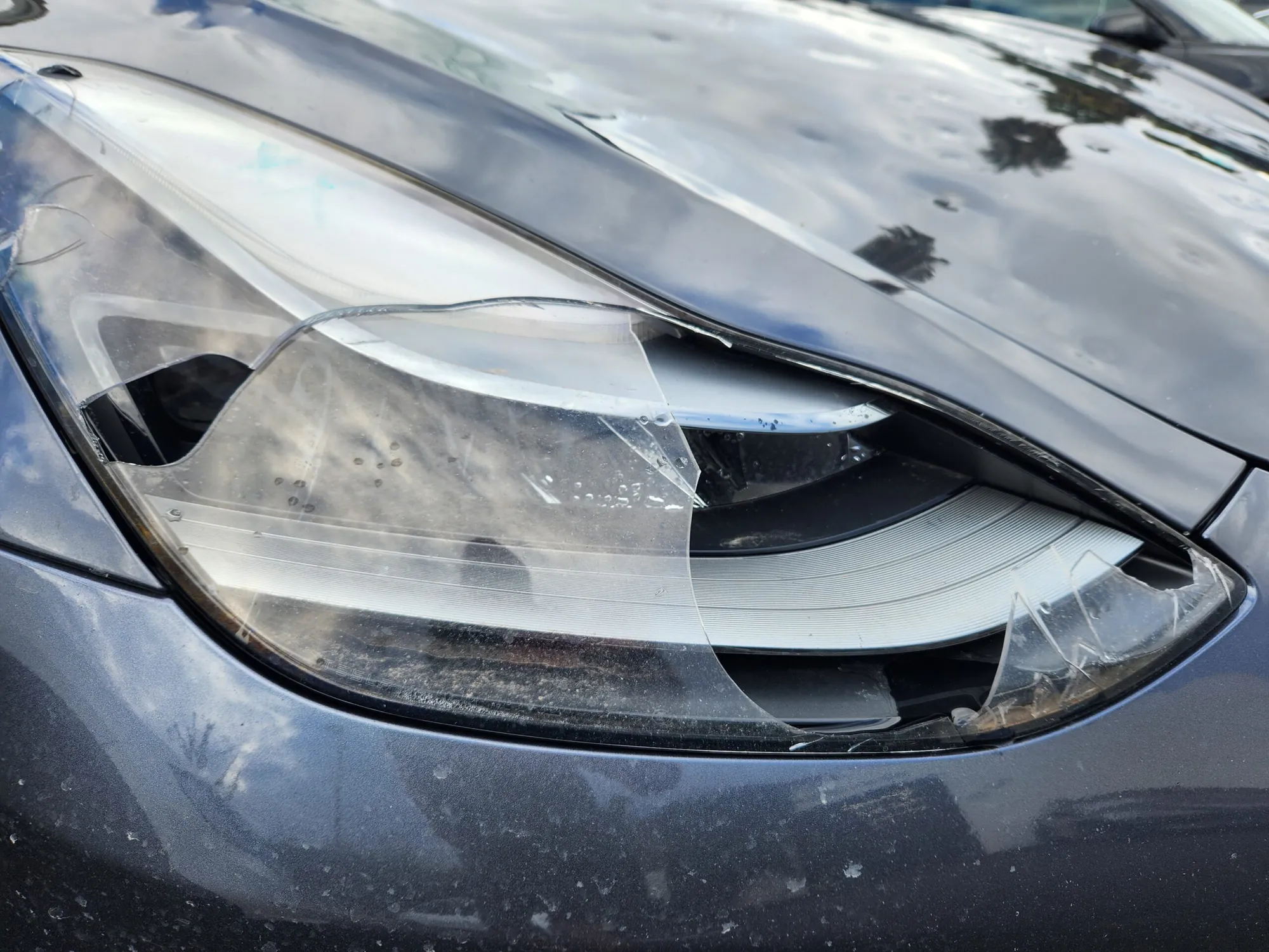 Cracked headlight lens on gray Tesla Model 3 before replacement at TSK