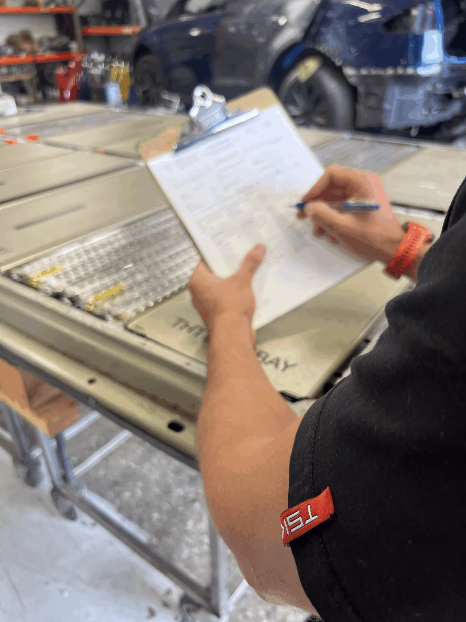 Technician documenting Tesla Model 3 battery inspection on a clipboard checklist