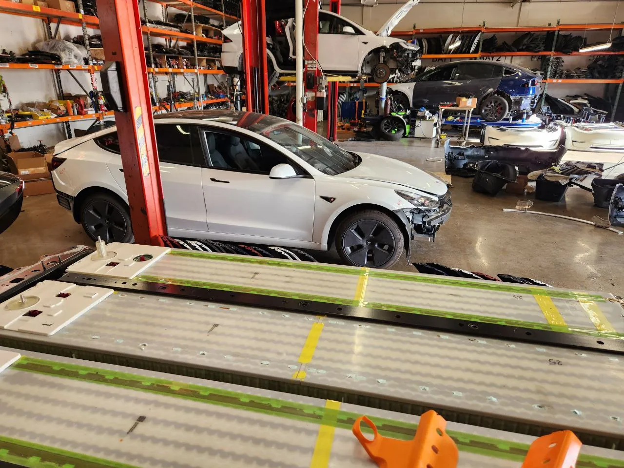 Tesla Model 3 undergoing front-end repair in TSK shop with battery pack in foreground