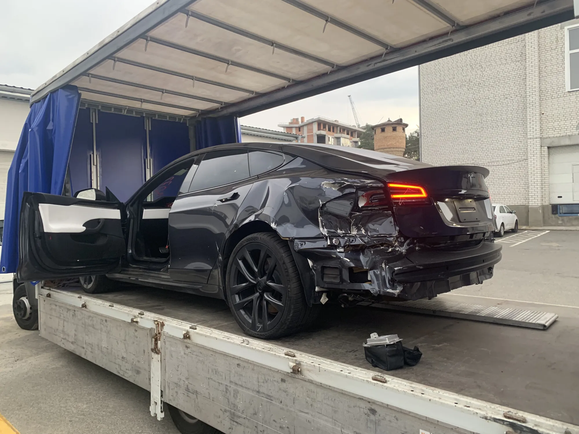 Black Tesla Model S with rear-end collision damage loaded on flatbed trailer