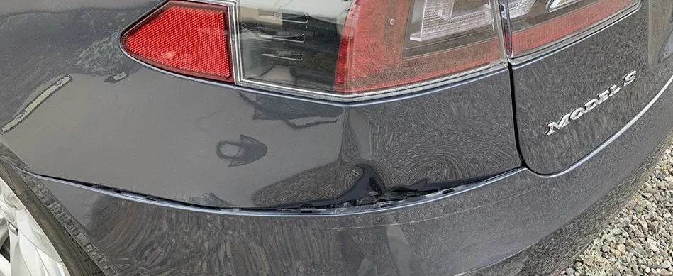 Close-up of dent and paint damage on Tesla Model S rear bumper edge