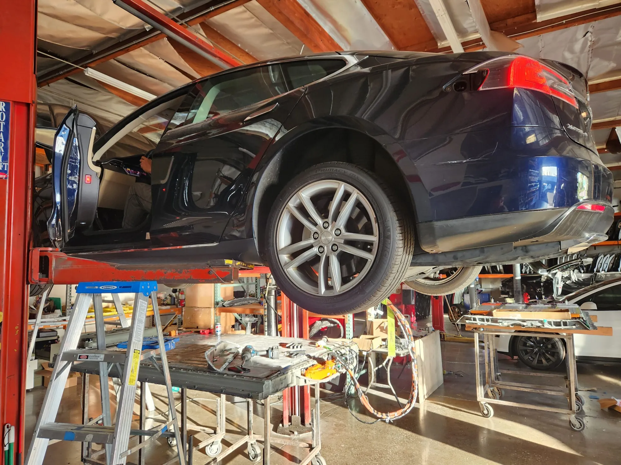 Black Tesla Model S raised on lift for battery diagnostics at TSK repair shop