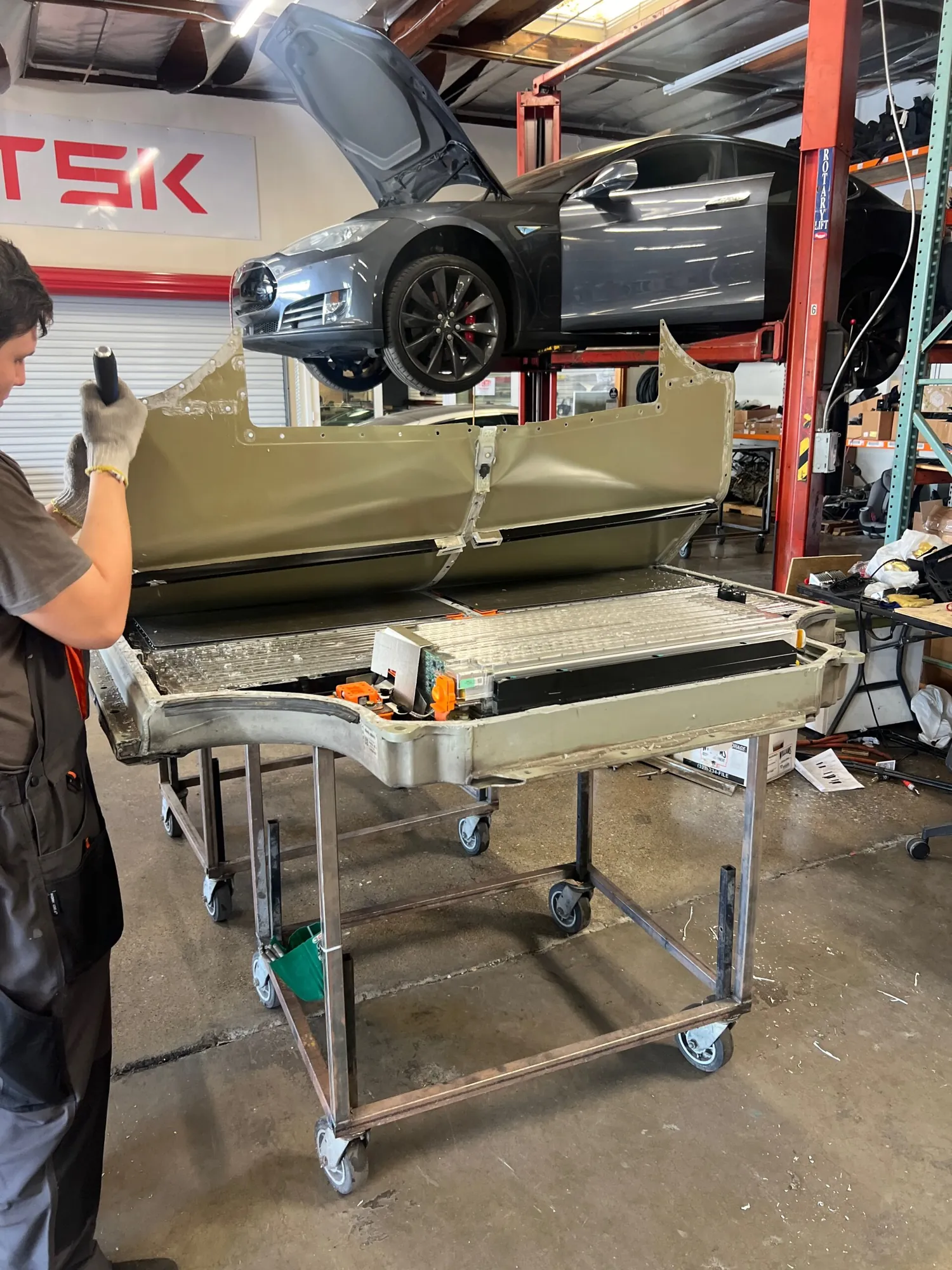 Technician inspects Tesla Model S battery pack removed on cart at TSK shop