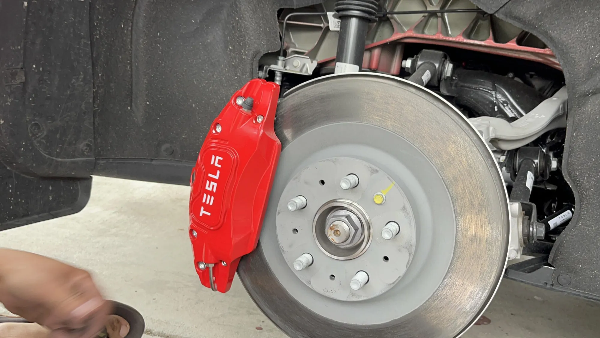 Red Tesla brake caliper and rotor exposed during Model S suspension repair at TSK