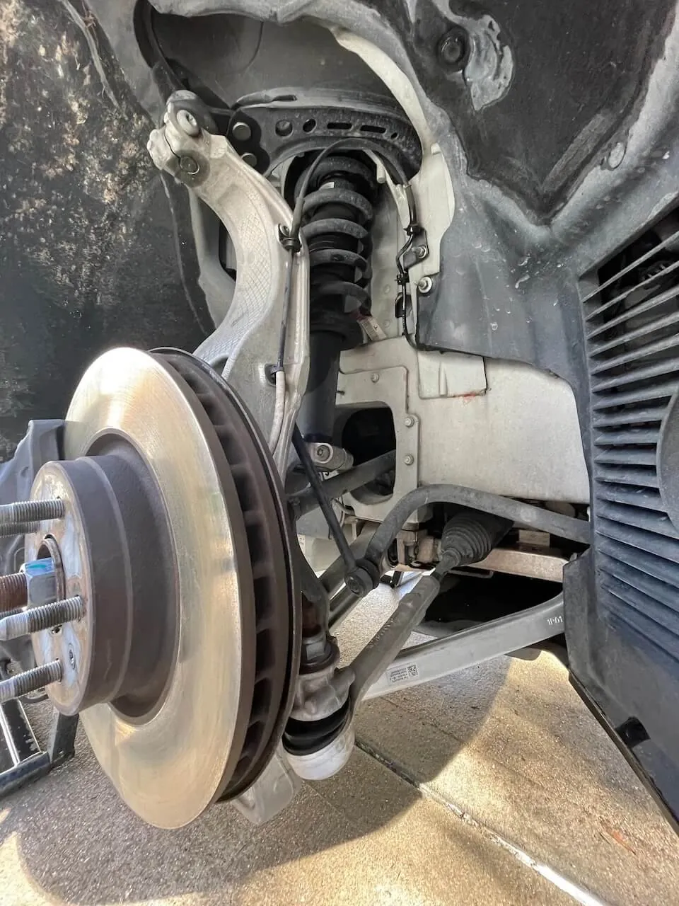 Tesla Model S front suspension with brake rotor, coil spring, and control arms exposed