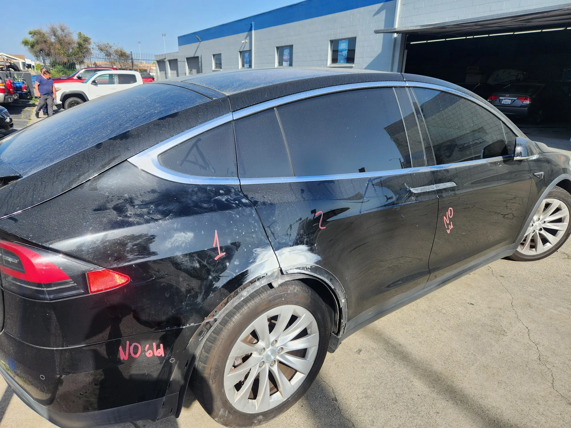 Black Tesla Model X with rear quarter panel damage marked for aluminum body repair