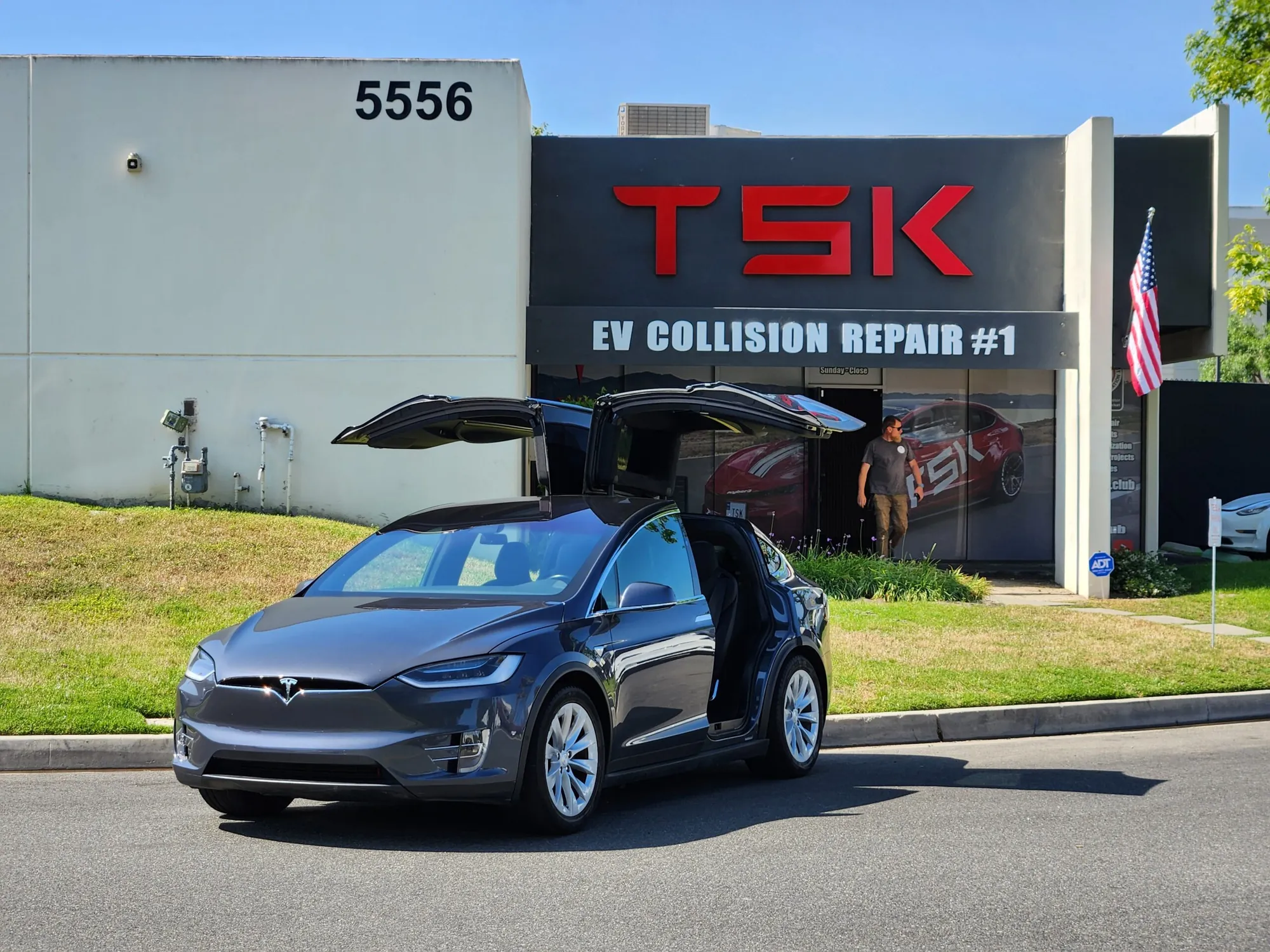 Gray Tesla Model X with falcon-wing doors open outside TSK EV Collision Repair shop