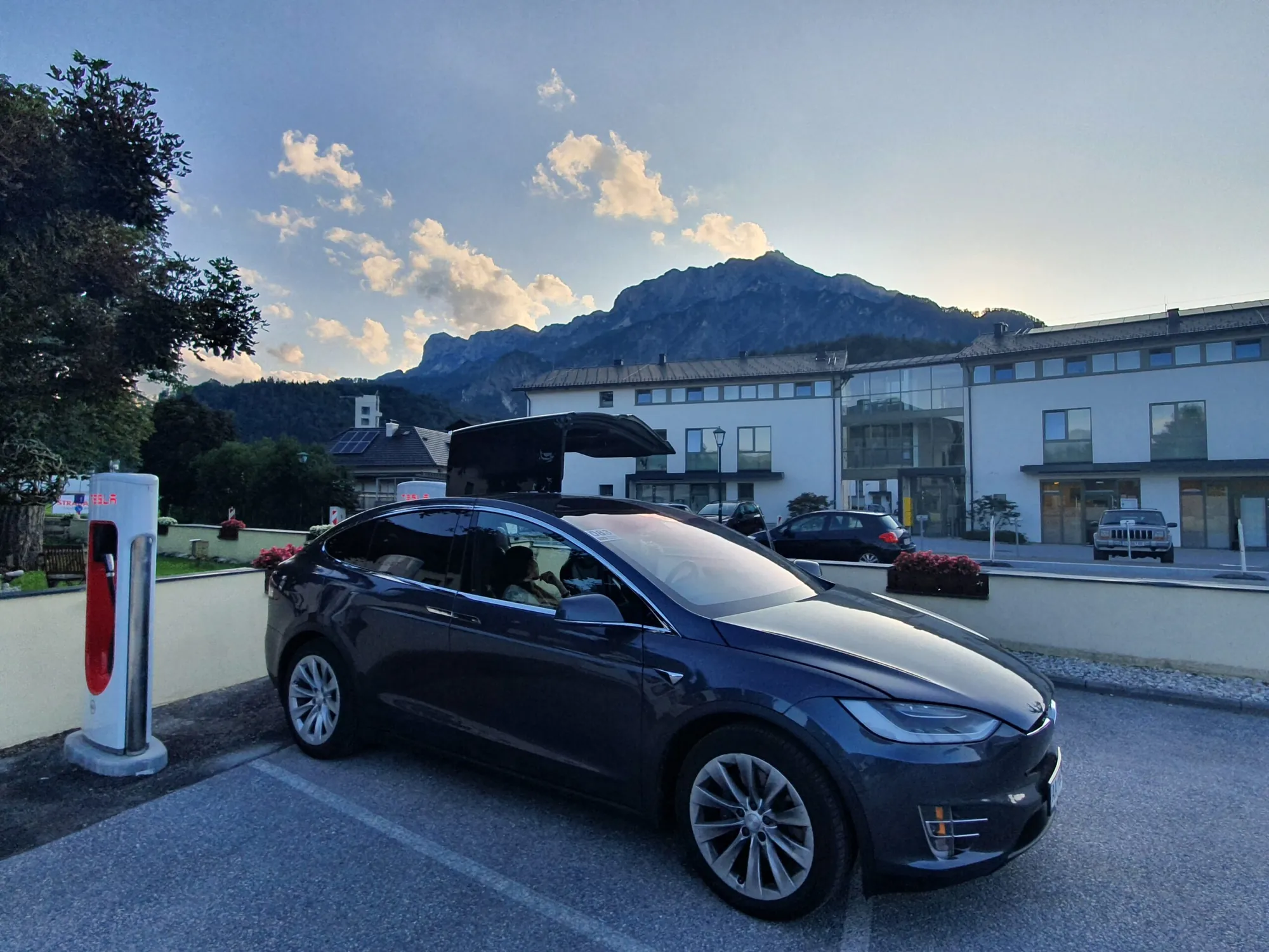 Tesla Model X with falcon-wing door open charging at a Supercharger station