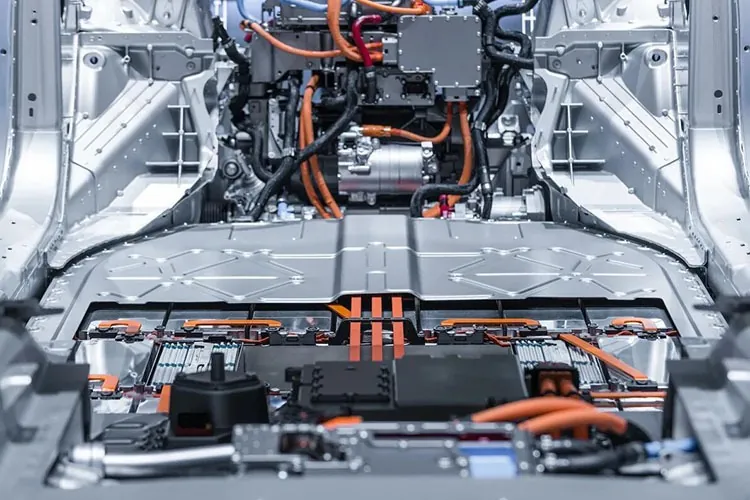 Tesla Model X underbody exposing battery pack, orange high-voltage cables, and charging components