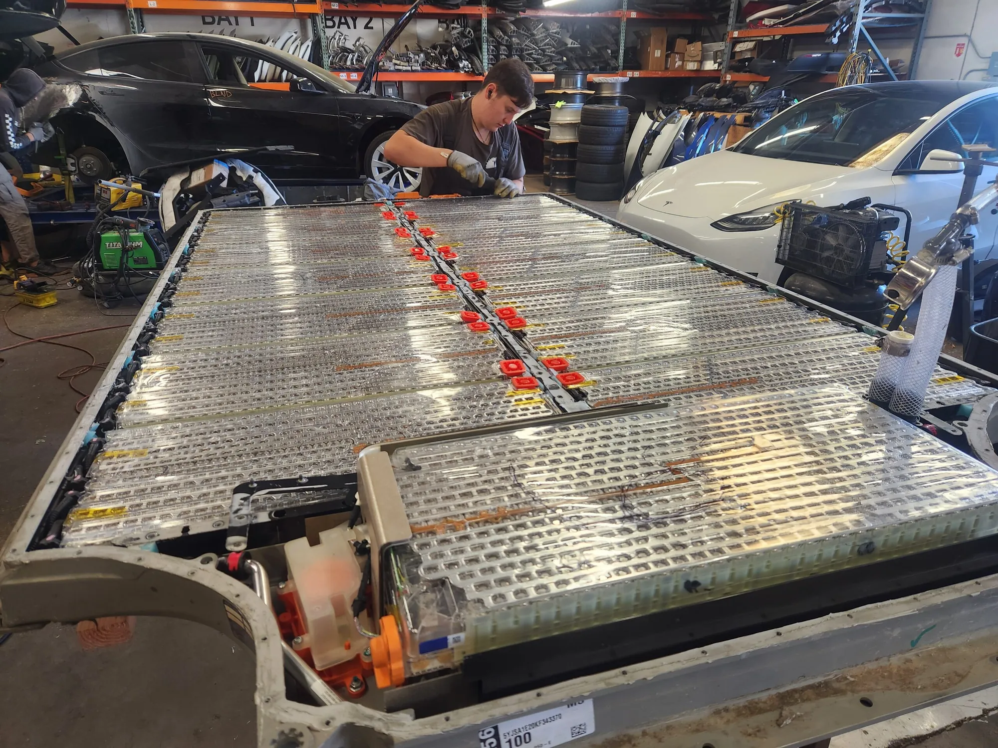 Technician inspecting exposed Tesla Model X high-voltage battery pack cells at TSK
