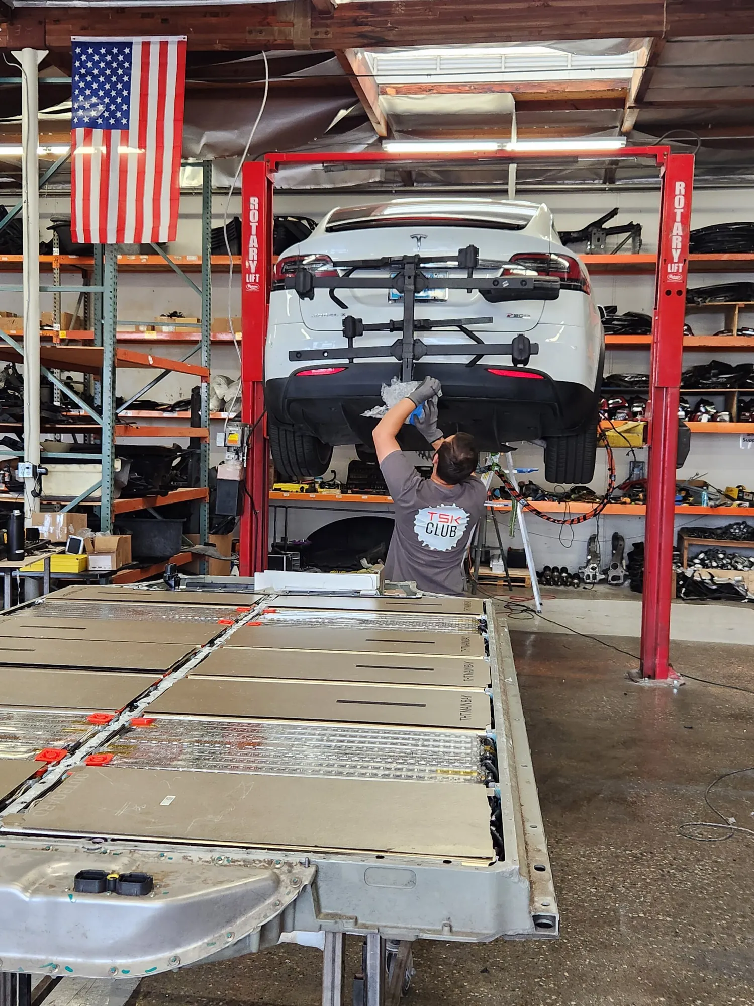 Technician working under raised Tesla Model X with battery pack removed at TSK