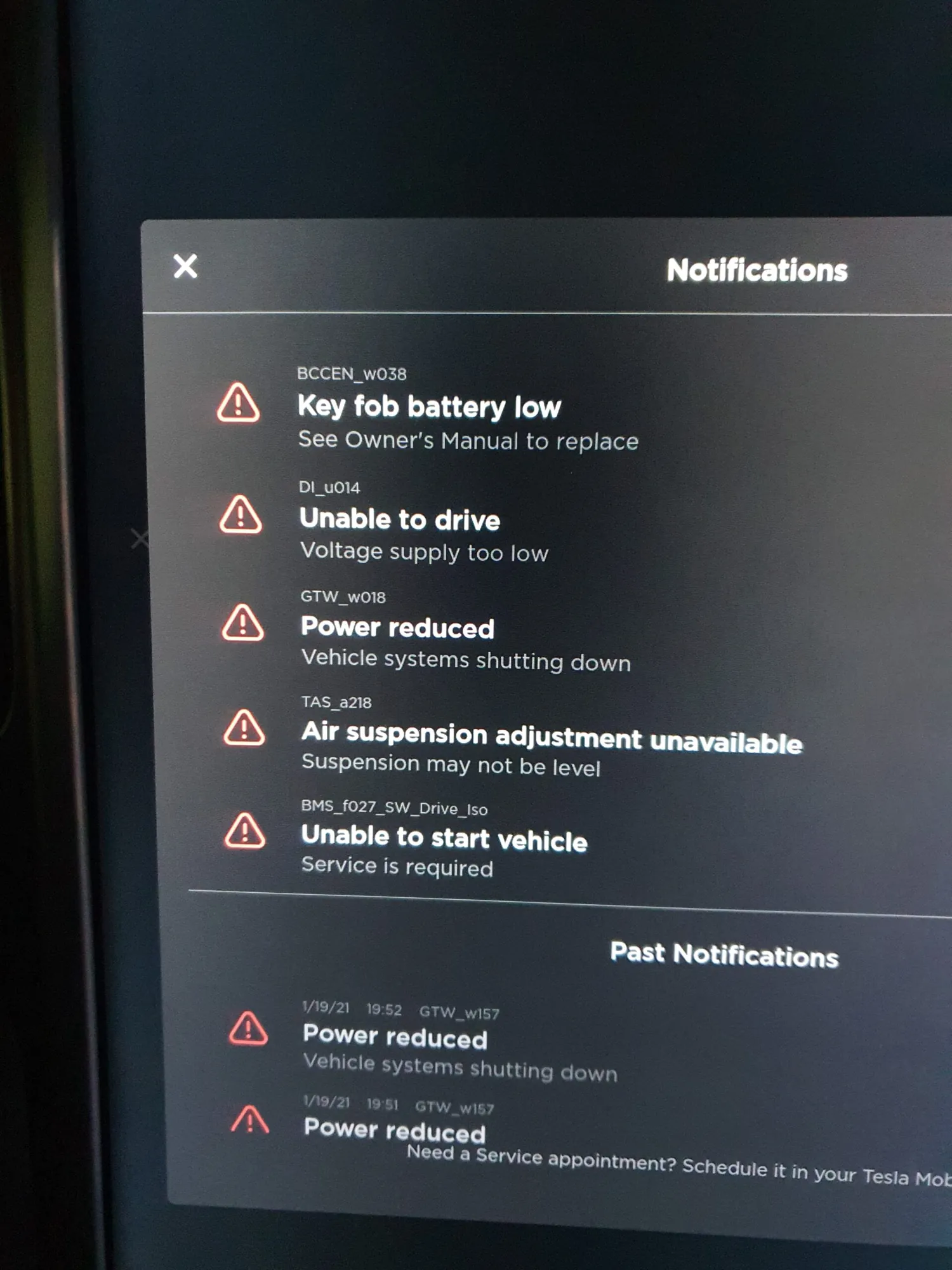 Tesla touchscreen showing multiple system notifications, including low voltage and service alerts
