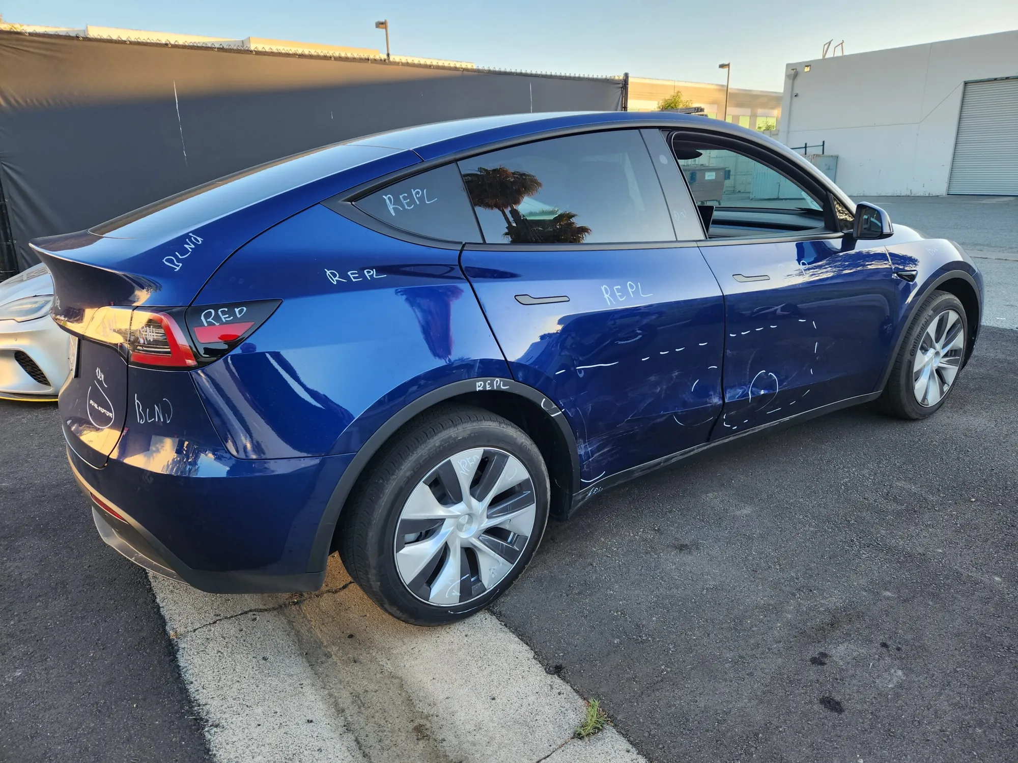 Blue Tesla Model Y with repair markings on door, quarter panel, and bumper at TSK