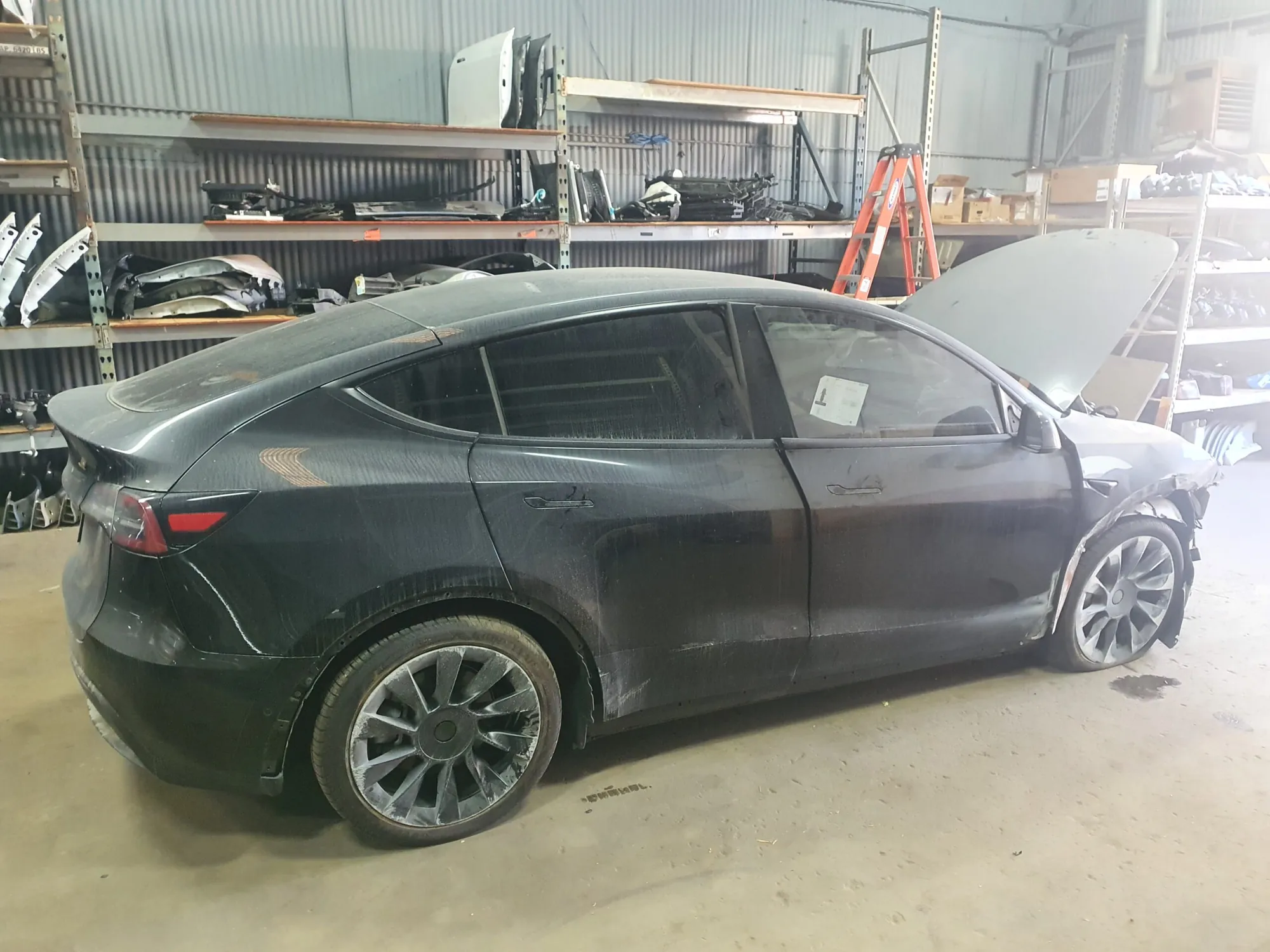 Black Tesla Model Y with front-end damage in TSK collision repair shop