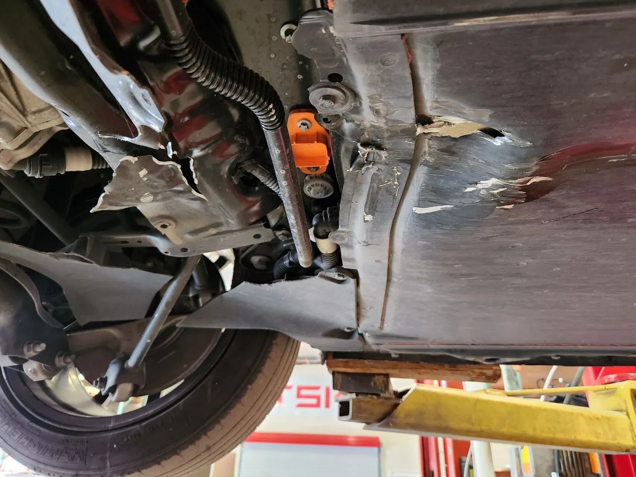 Underside of Tesla Model Y showing battery pack damage and orange high-voltage connector