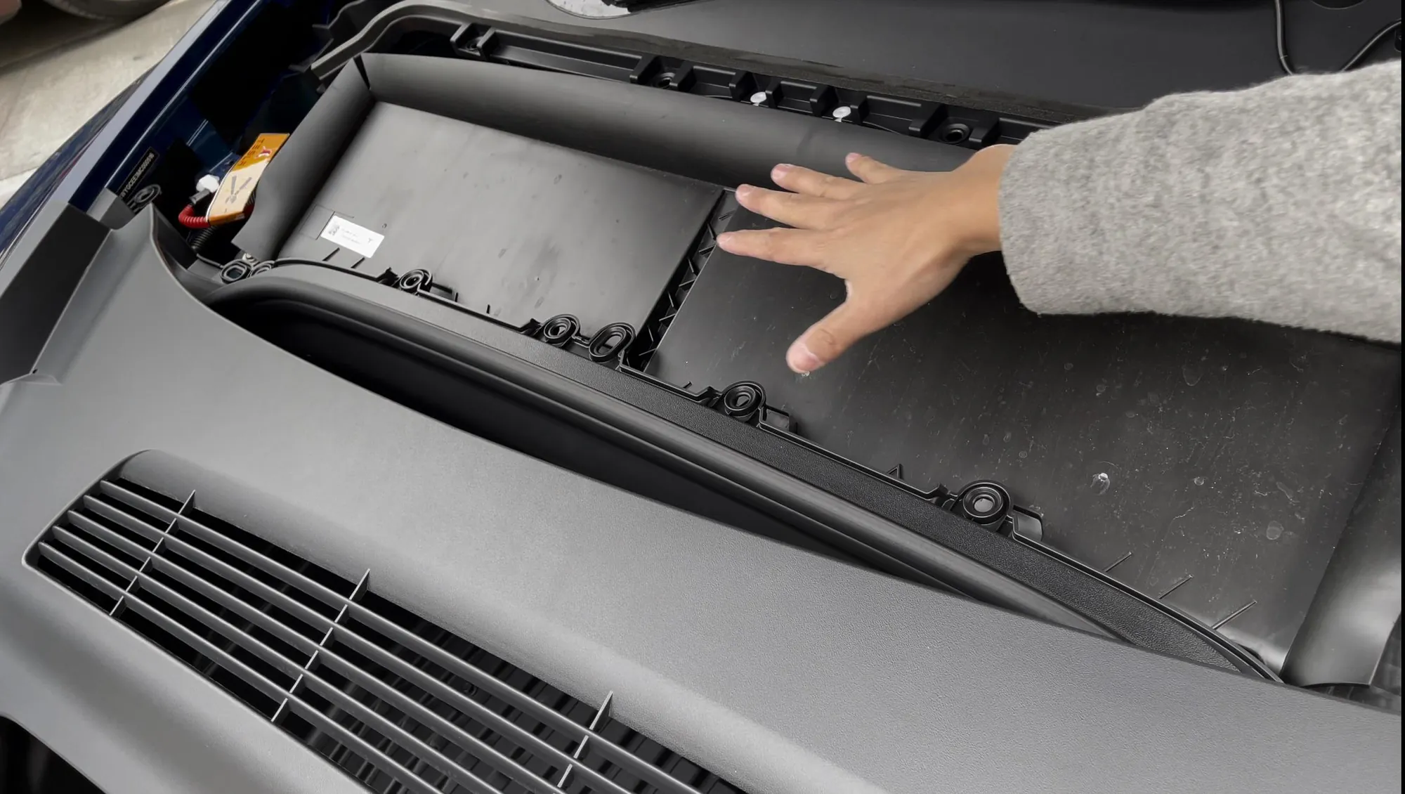 Technician accessing Tesla Model Y cabin air filter compartment under the hood