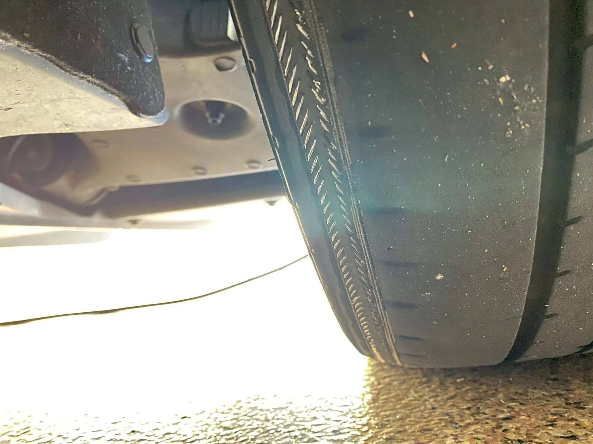Close-up of Tesla Model Y rear tire tread and underbody during suspension inspection at TSK