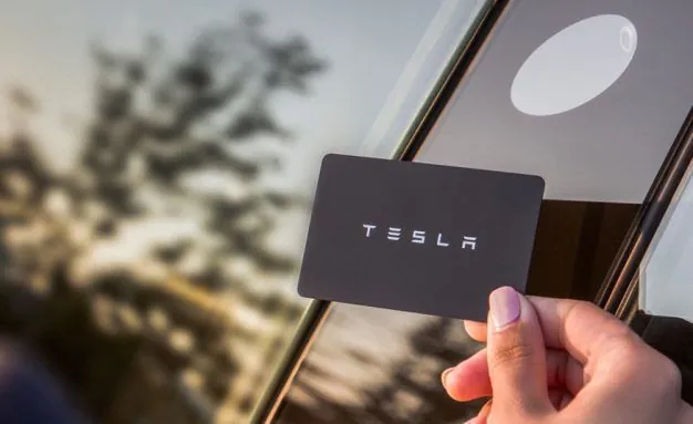 Hand holding Tesla key card near vehicle window for key programming service