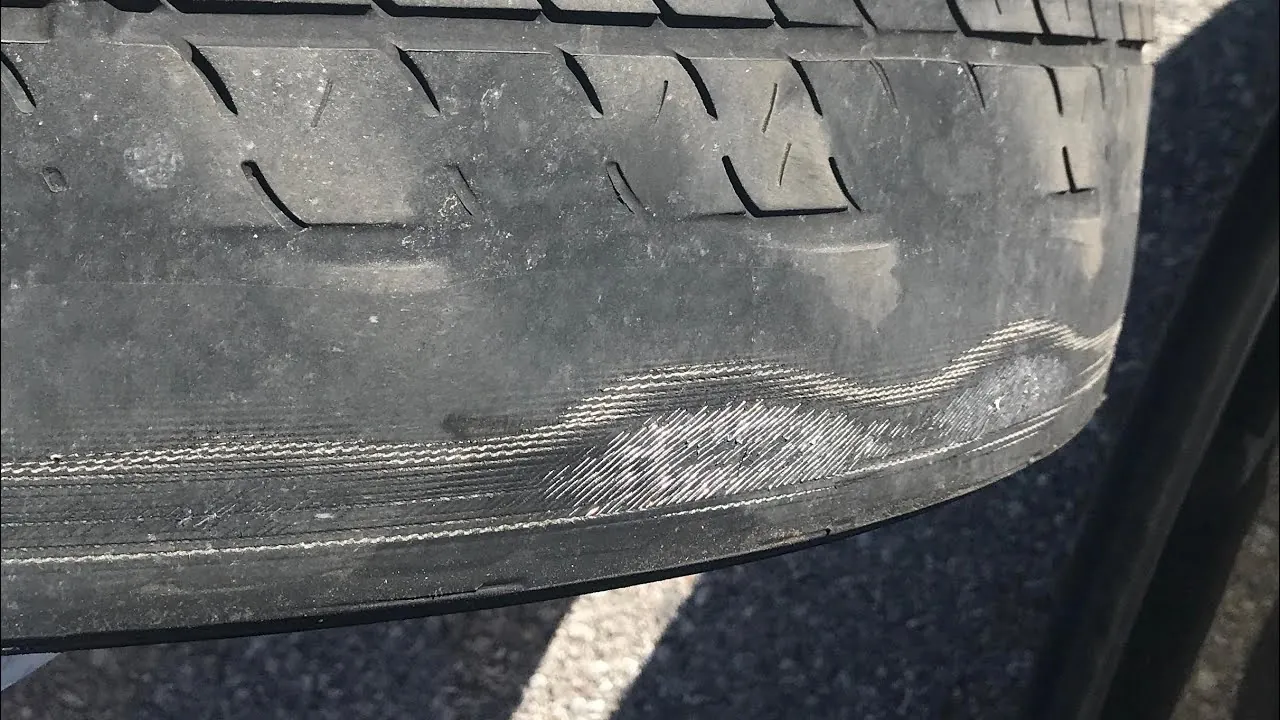 Close-up of curb rash and scuffed tire sidewall indicating suspension alignment wear