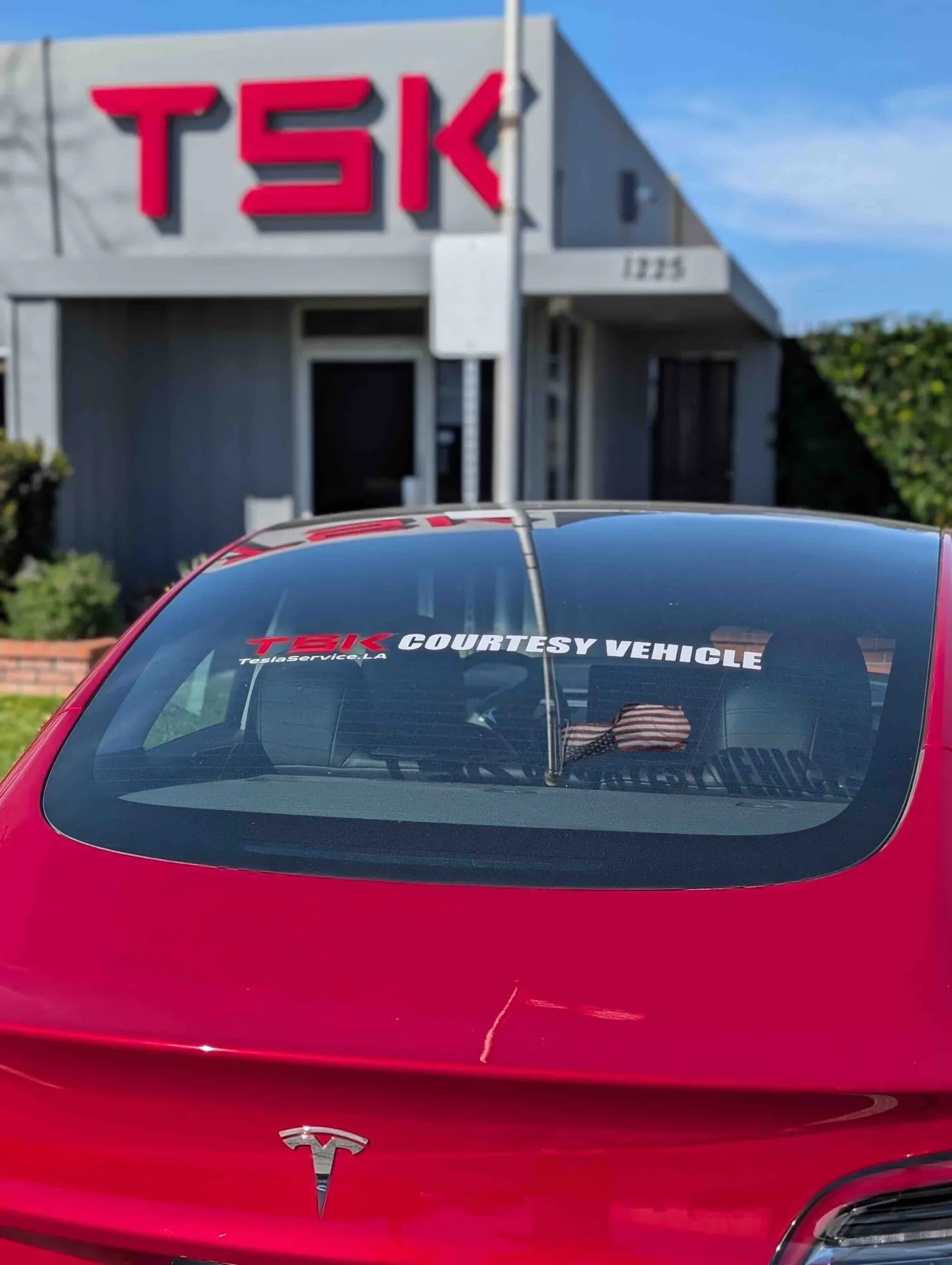 Red Tesla courtesy vehicle parked outside TSK shop with logo sign