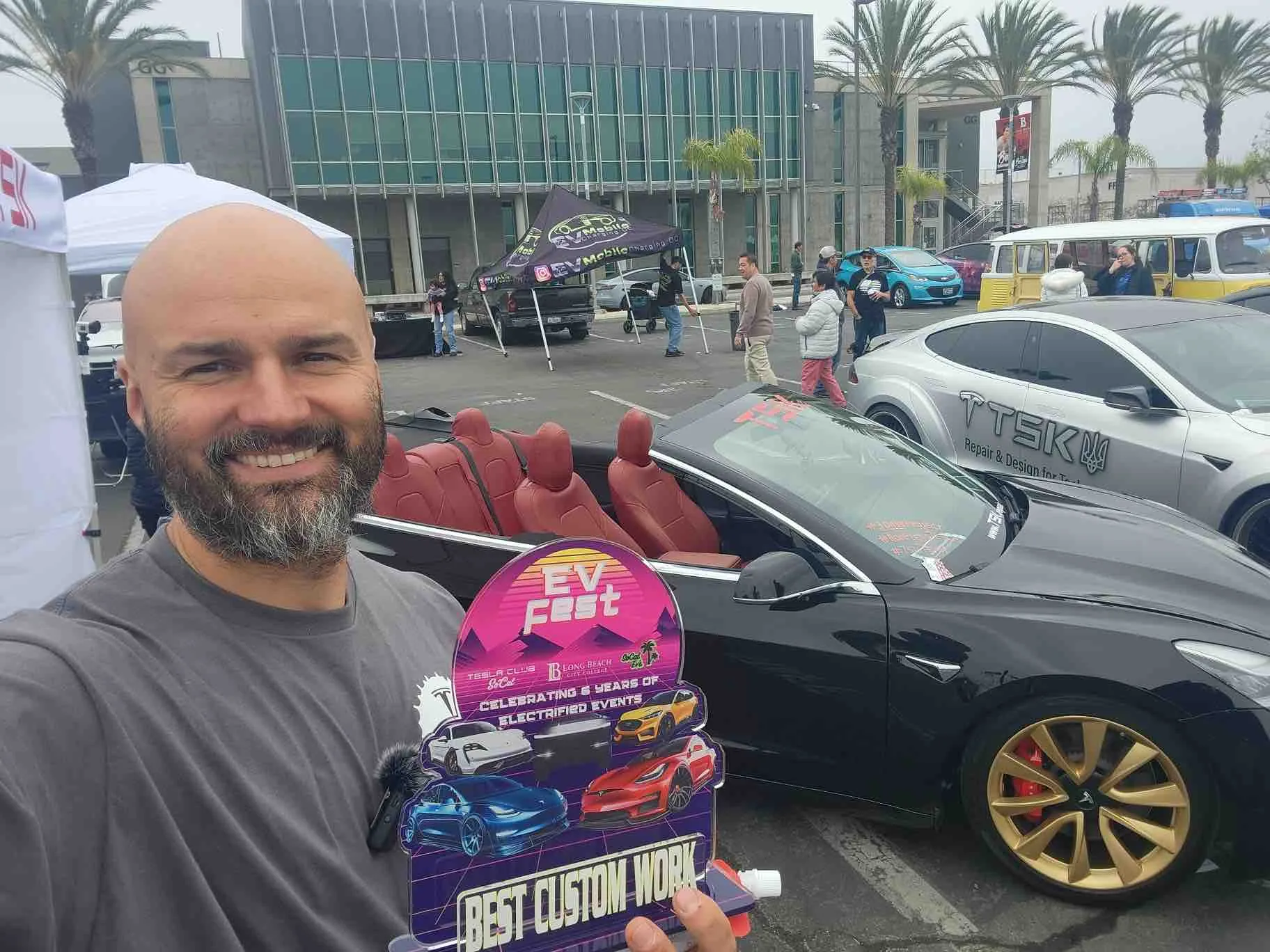 TSK team member holding EV Fest Best Custom Work award beside custom Tesla convertible