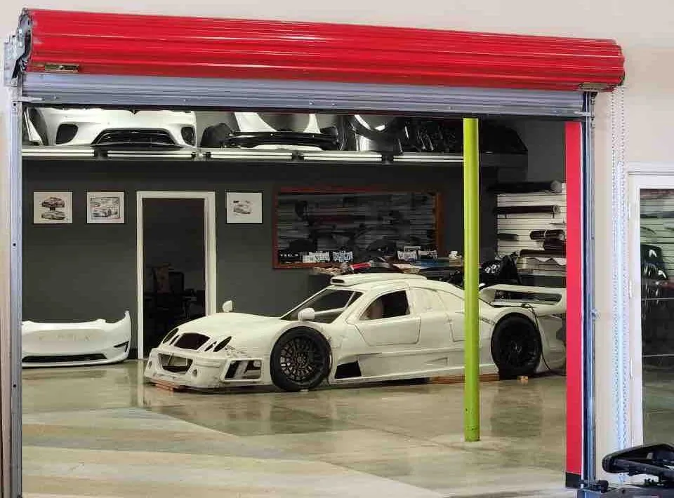 White custom race car body shell under open shop door at TSK