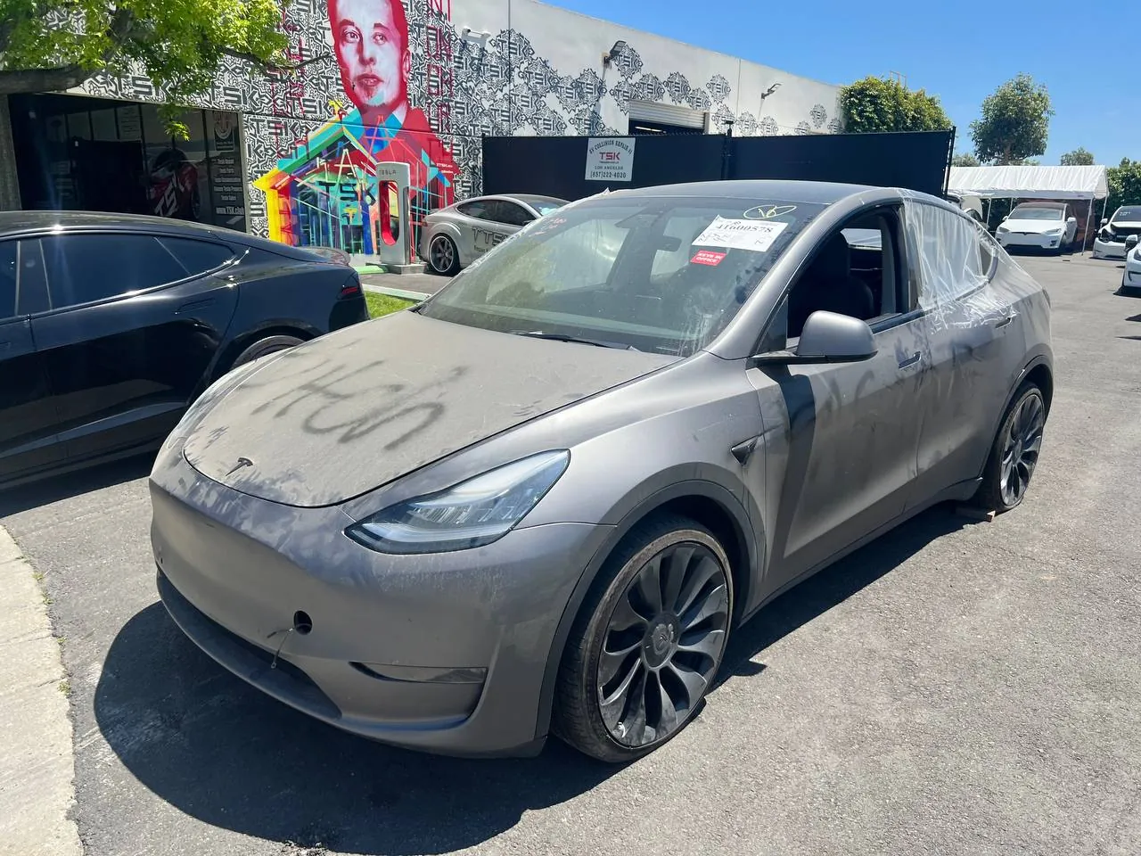 Vandalized gray Tesla Model Y with spray paint, shattered window at TSK