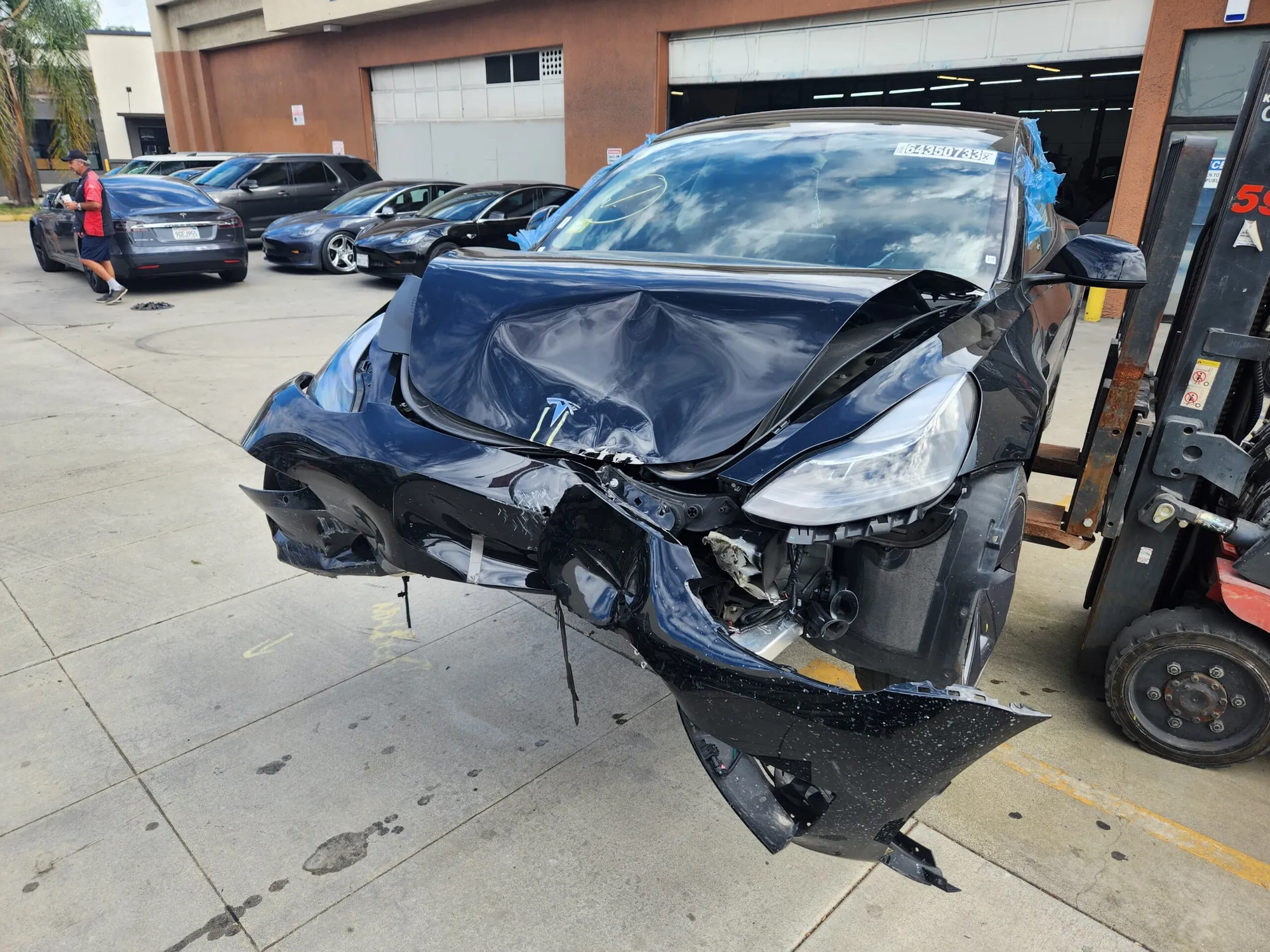 Black Tesla Model 3 with severe front-end collision damage at TSK body shop