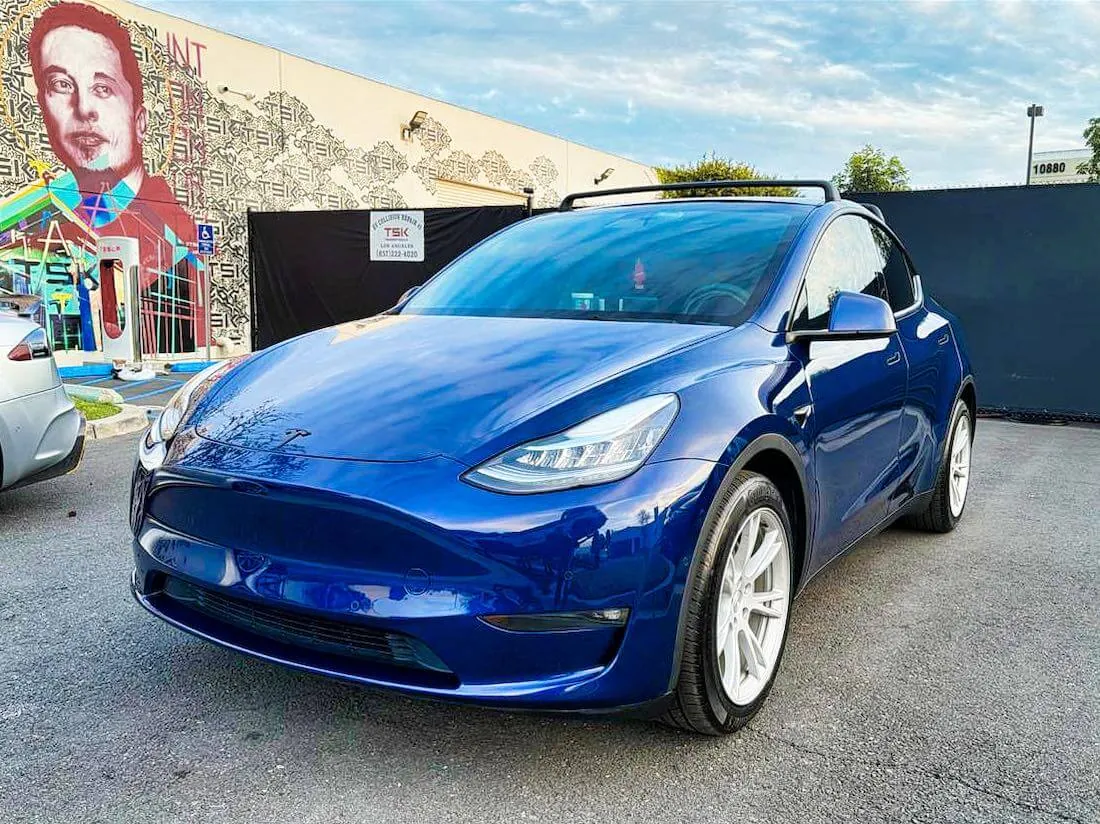 Blue Tesla Model Y parked outside TSK EV collision repair shop with mural