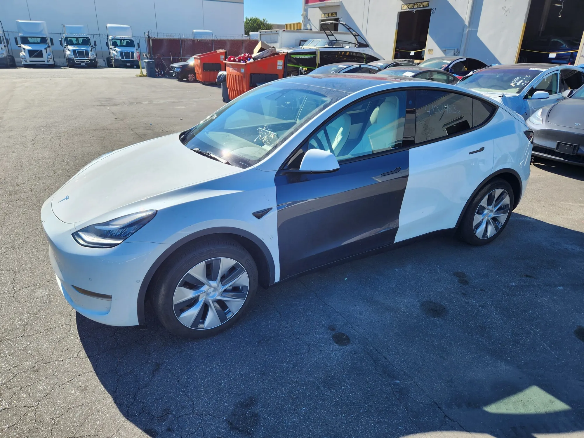 White Tesla Model Y with unpainted primer door panel awaiting bodywork repair