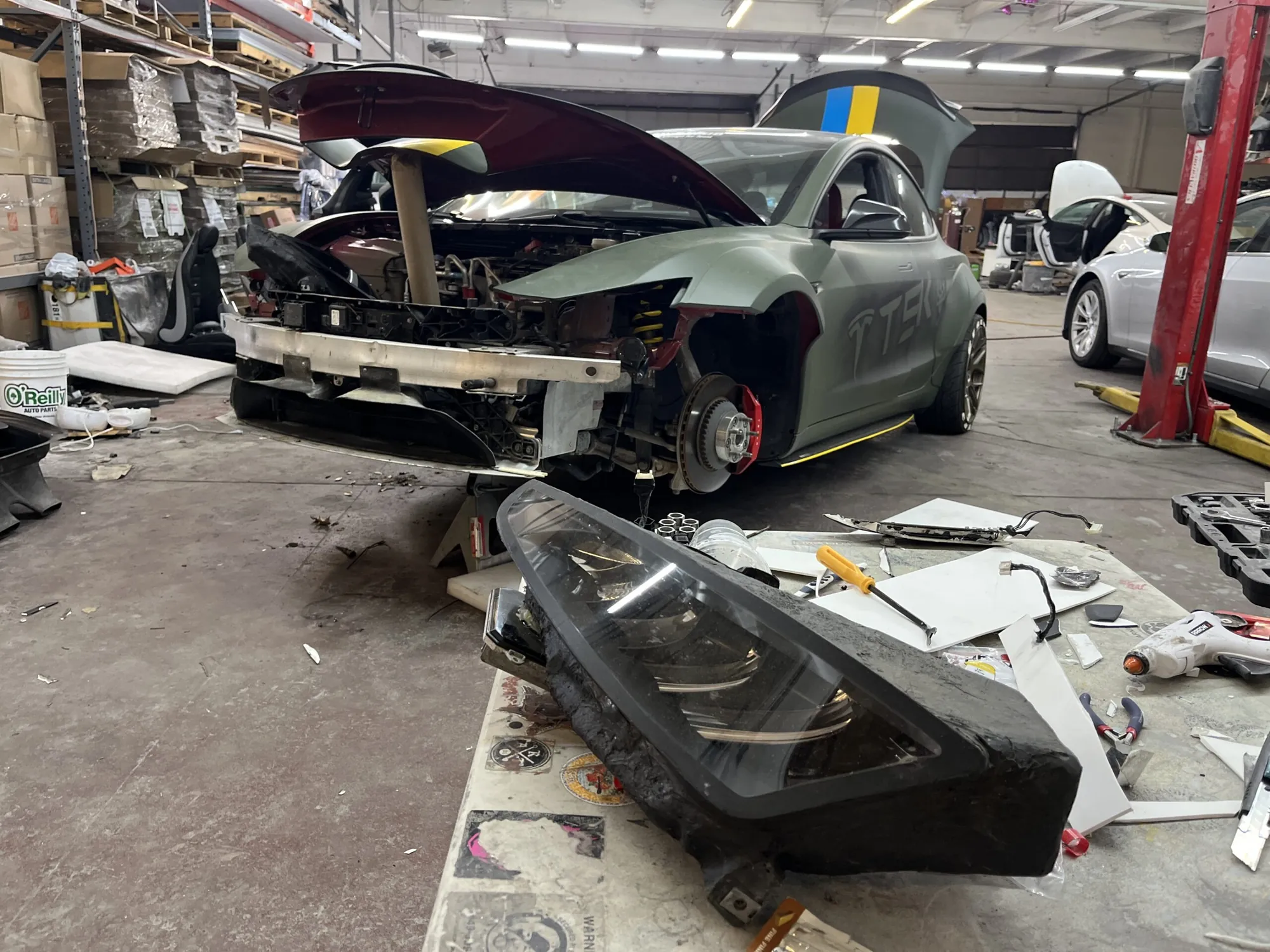 Tesla Model 3 with front bumper removed, headlight assembly on shop table