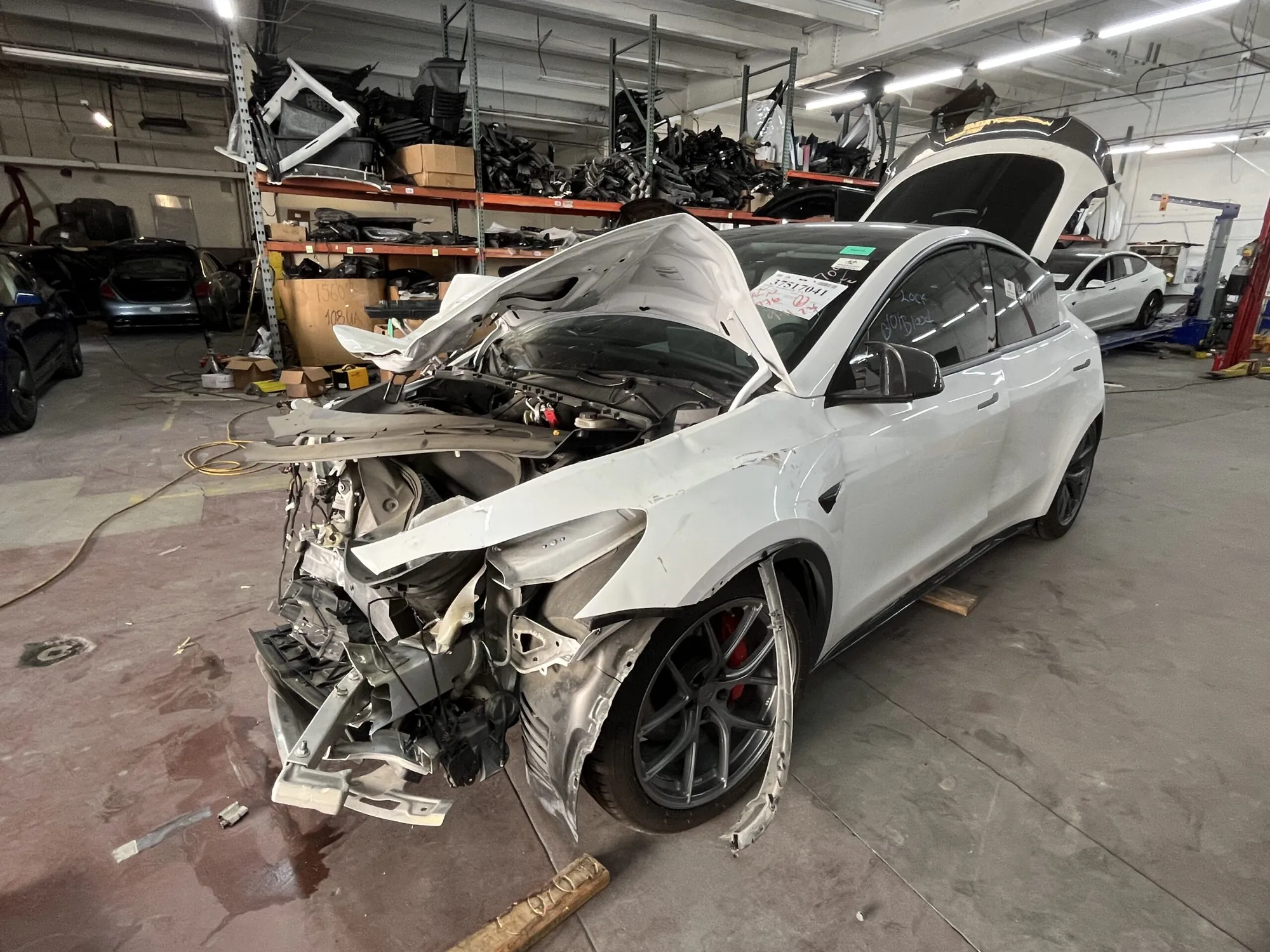 White Tesla Model Y with severe front-end collision damage in TSK repair shop