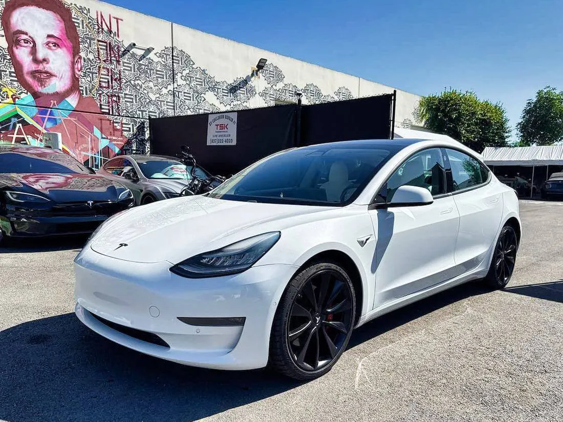 White Tesla Model 3 with black wheels parked outside TSK EV collision repair shop